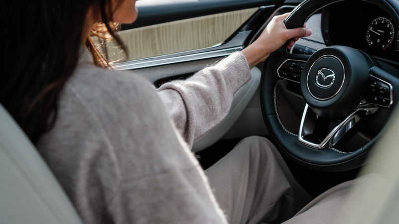 Un conducteur vêtu d’un chandail de laine, les mains sur le volant, à l’intérieur d’un CX-90.   