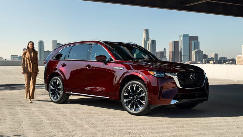 Un conducteur en costume havane ouvre la portière pour sortir d’un VÉHR CX-90 rouge artisan. 